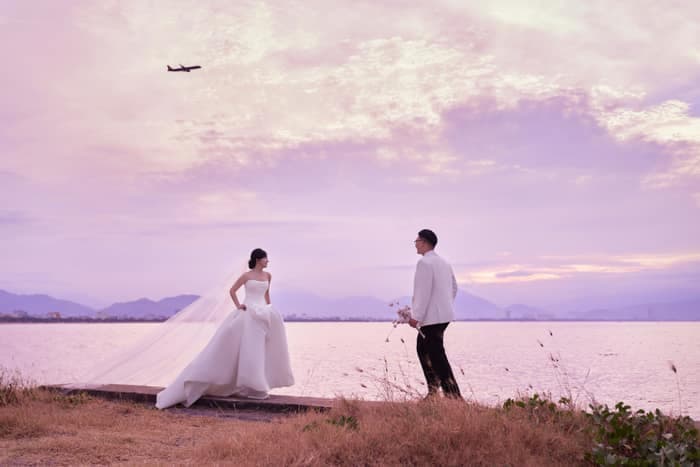Bride and groom standing by the lake under a pink sky
