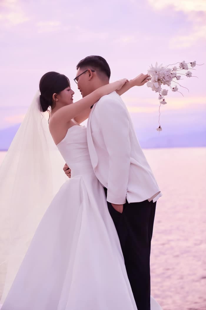 Bride and groom holding glasses beside a white classic car