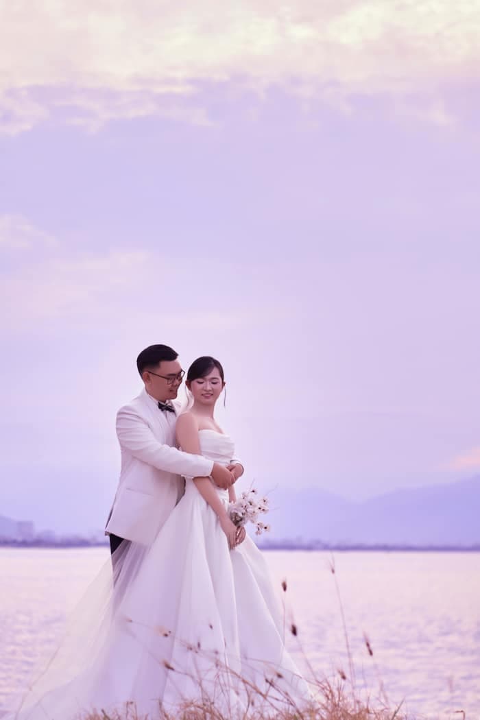 Bride and groom embracing by the sea at sunset