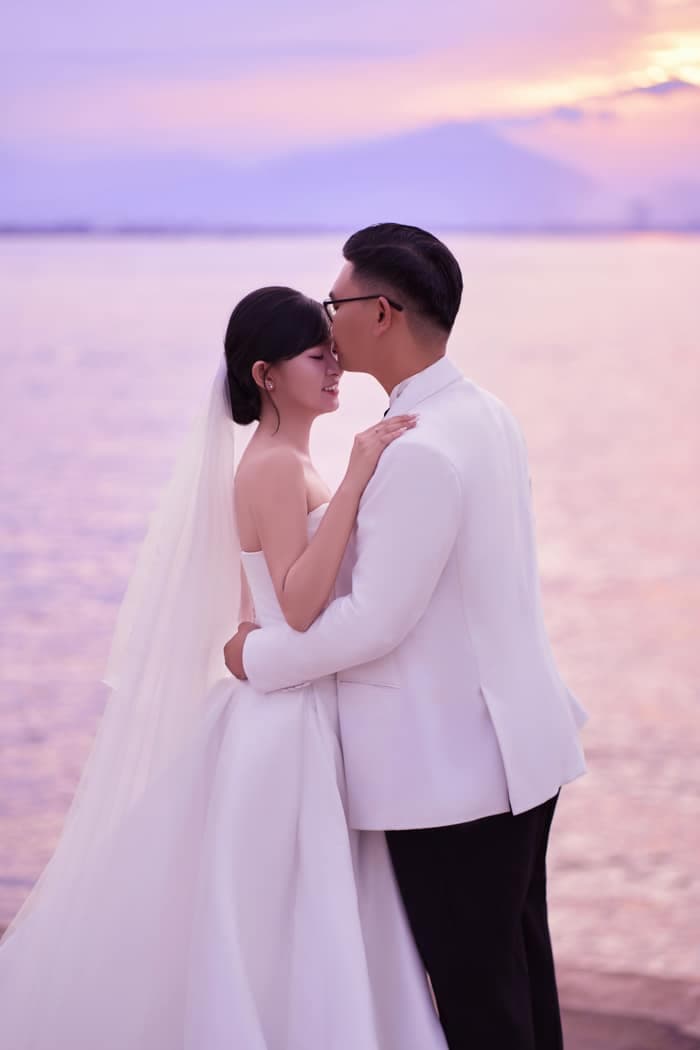 Groom kissing bride on the forehead by the sea